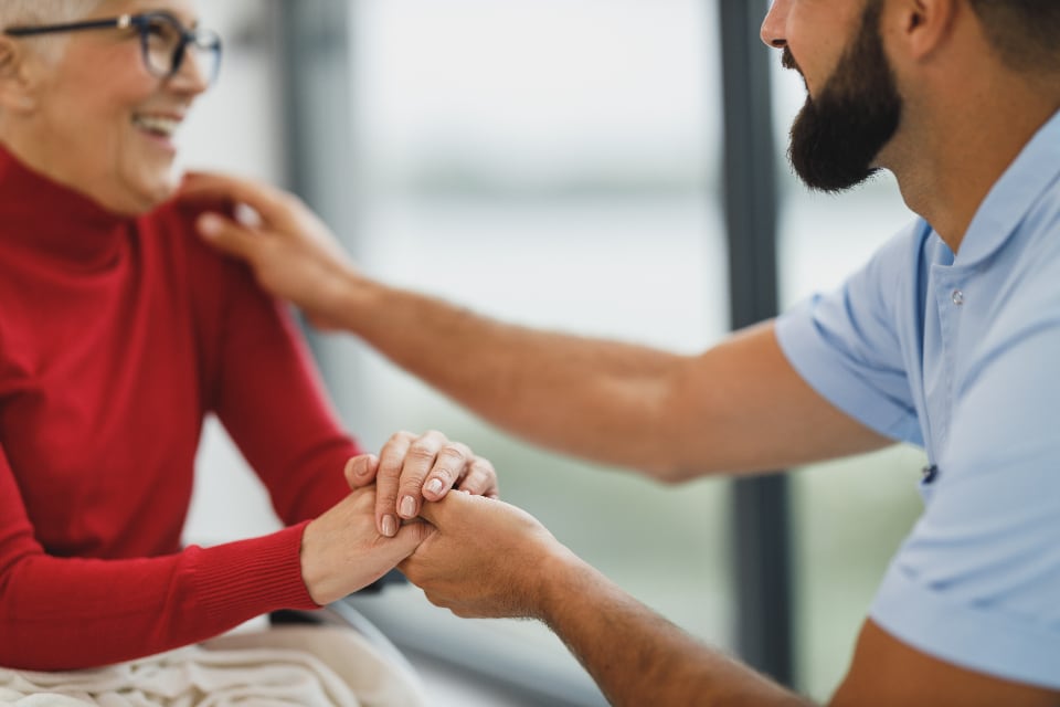 A support worker holding the hands of a smiling older woman