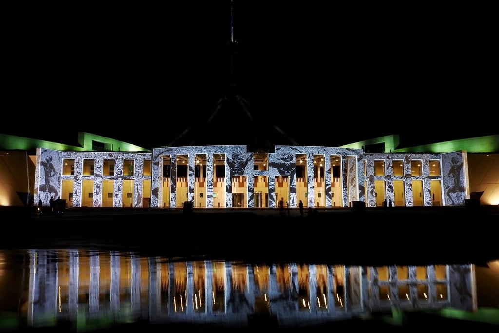 Parliament House in Canberra at night, its facade lit with projections and reflected in the forecourt pool